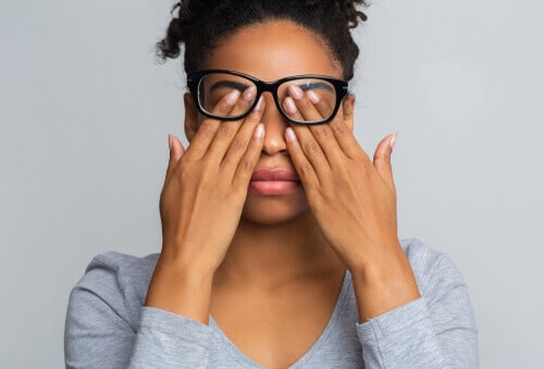 Young woman rubbing eyes under glasses.